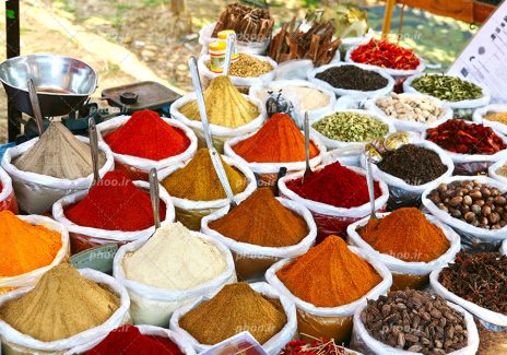 عکس با کیفیت انواع ادویه های رنگارنگ در کنار یکدیگر و قاشق های نقره ای در آنها