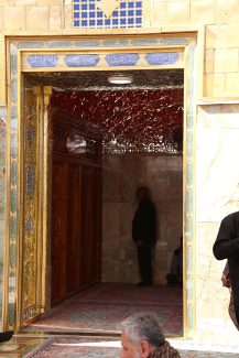 عکس با کیفیت طرح یا پوستر حرم مطهر امام علی (ع) و مرد در حال نمار خواندن در صحن و در طلایی و کتیبه های طلایی بر روی آن