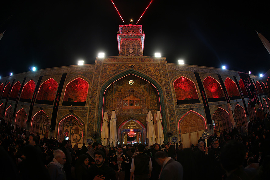 عکس با کیفیت طرح یا پوستر حرم مطهر امام علی (ع) تصویر گرفته شده از حرم مطهر به صورت پرسپکتیو از مقابل باب الساعه در شب های قدر و چراغ های قرمز و حضور مردم در حرم برای مراسم احیا