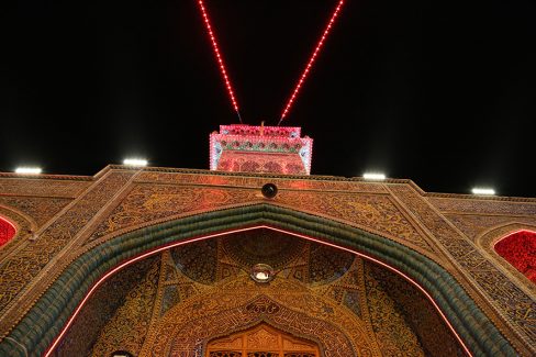 عکس با کیفیت طرح یا پوستر حرم مطهر امام علی (ع) گلدسته ای در بالای صحن باب الساعه و چراغ های قرمز وصل شده به آن و تصویر گرفته شده از زاویه پایین