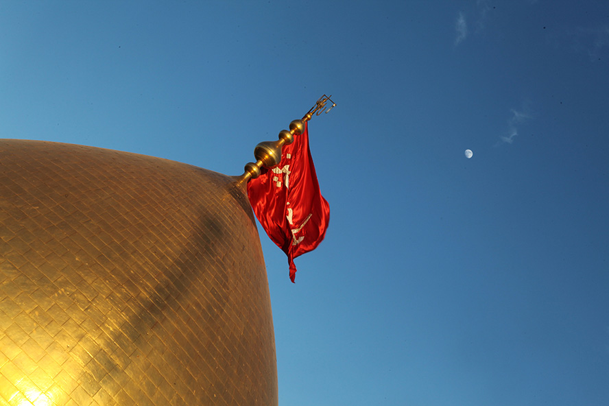 عکس با کیفیت پرچم قرمز رنگ وصل به گنبد طلایی و آسمان آبی در پس زمینه