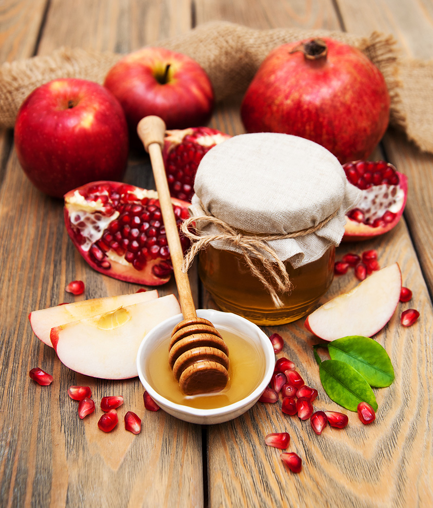عکس با کیفیت طرح یا پوستر شب یلدا پارچه کنفی بر روی میز و در پشت انار و سیب و اسلایس های سیب و انار در کنار ظرف شیشه ای عسل و قاشق عسل خوری در ظزف سفید رنگ حاوی عسل و برگ های سبز در کنار ظرف
