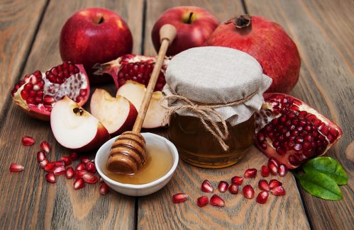 عکس با کیفیت طرح یا پوستر شب یلدا دانه های انار در کنار ظرف های عسل و اسلایس های سیب و انار در کنار انار و سیب های پشت ظرف و قاشق عسل خوری در ظرف