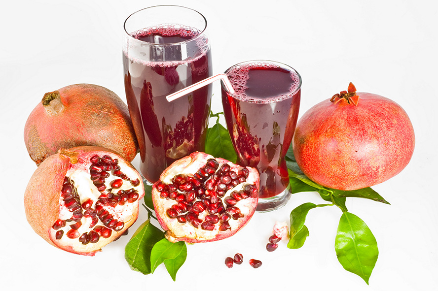 عکس با کیفیت طرح یا پوستر شب یلدا آب انار در لیوان های بلند شیشه ای بر روی برگ های سبز و انار های کامل و اسلایس شده در کنار لیوان ها بر روی پس زمینه سفید