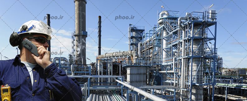 عکس با کیفیت مرد با لباس های سرمه ای و عینک آفتابی و کلاه ایمنی سفید در حال صحبت کردن با تلفن همراه بر روی سکوی نفتی