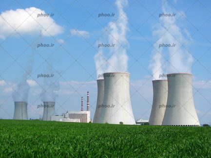 عکس با کیفیت نیروگاه های حرارتی بر روی چمن ها و دود در حال خارج شدن از بالای آنها و پس زمینه آسمان ابری و آبی