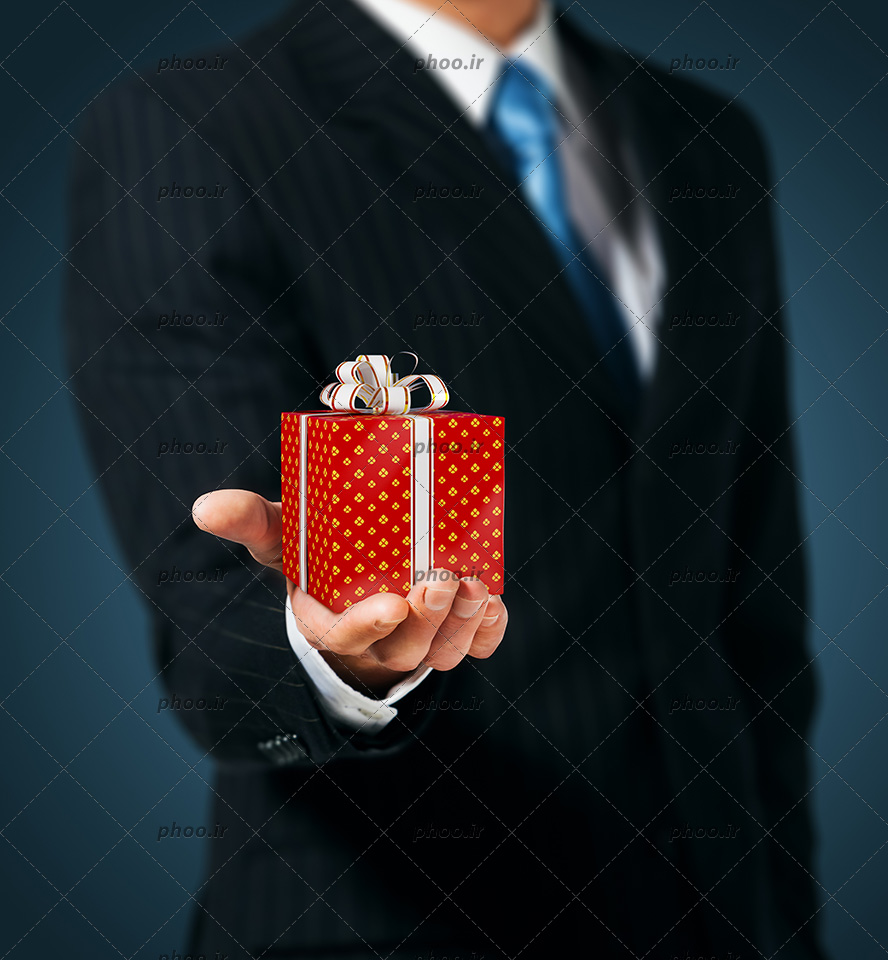 عکس با کیفیت جعبه کادو زیبا به رنگ قرمز در دست مرد با کت و شلوار مشکی
