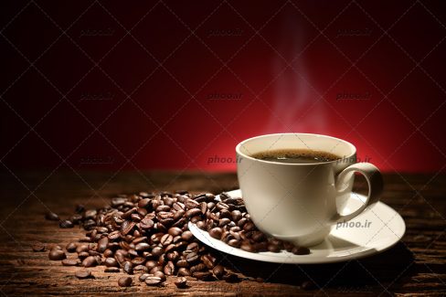 عکس با کیفیت پس زمینه به رنگ قرمز و فنجان قهوه به رنگ سفید در کنار دانه های قهوه