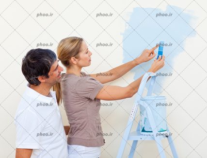 عکس با کیفیت زن و مرد ایستاده در کنار نردبان و سطل رنگ و در حال انتخاب رنگ برای دیوار