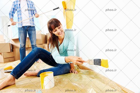 عکس با کیفیت زن و مرد در حال رنگ زرد زدن به دیوار به کمک قلمو و غلتک