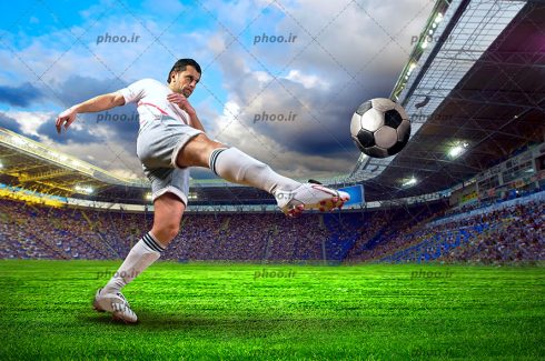 عکس با کیفیت فوبالیست با لباس ورزشی سفید در حال شوت کردن توپ فوتبال به سمت تماشاگرها