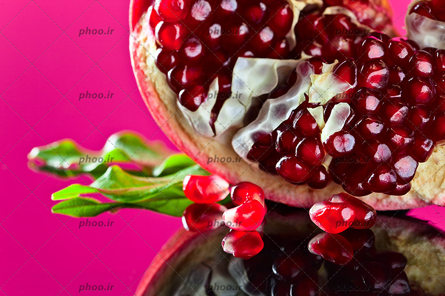 عکس با کیفیت انار دانه یاقوتی همراه با برگ سبز و پس زمینه به رنگ صورتی