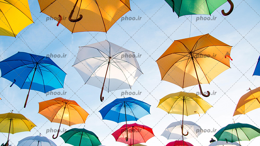 عکس با کیفیت چتر های رنگارنگ در کنار یکدیگر و آسمان در پس زمینه