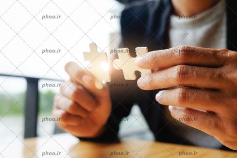 عکس با کیفیت دو تیکه پازل در دستان مرد با کت مشکی و پیراهن سفید و نور در بین قطعات پازل