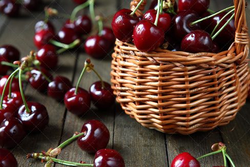 عکس با کیفیت سبد حصیری بر روی میز چوبی و گیلاس های چیده شده بر روی یکدیگر در سبد و چند گیلاس در اطراف سبد