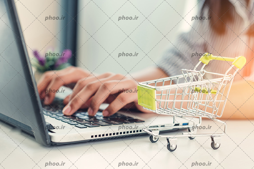 عکس با کیفیت زن در حال کار کردن با لپ تاپ و سبد چرخدار کوچک در کنار لپ تاپ
