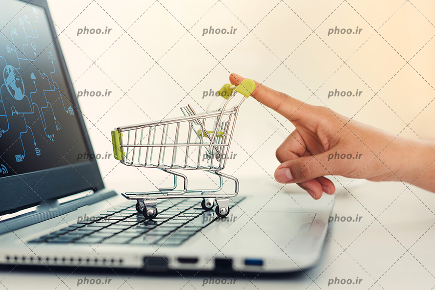 عکس با کیفیت سبد خرید چرخدار کوچک بر روی لپ تاپ و دست مرد بر روی سبد چرخدار