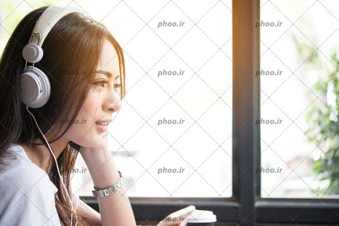عکس با کیفیت زن با چهره ی نیم رخ و در حال گوش دادن به آهنگ با هدفون سفید