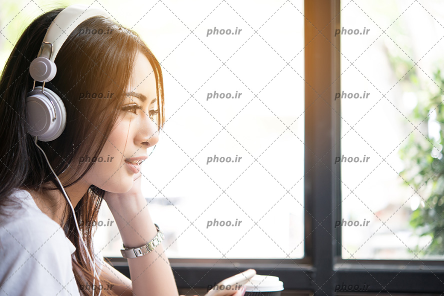 عکس با کیفیت زن با چهره ی نیم رخ و در حال گوش دادن به آهنگ با هدفون سفید