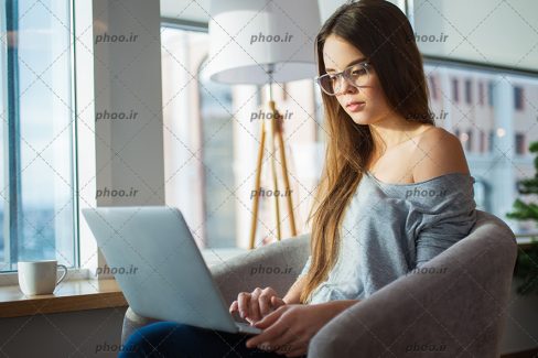 عکس با کیفیت زن نشسته بر روی صندلی در شرکت و در حال کار کردن با لپ تاپ