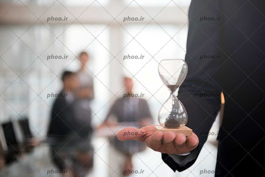 عکس با کیفیت ساعت شنی کوچک در دست مرد ایستاده با کت و شلوار
