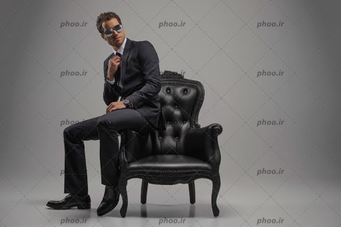 عکس با کیفیت مرد مدل با کت و شلوار مشکی نشسته بر روی دسته مبل زیبا