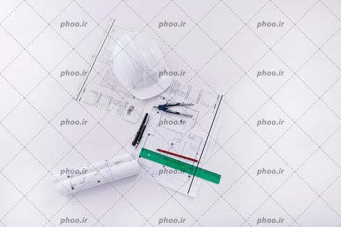 عکس با کیفیت کلاه ایمنی سفید بر روی نقشه های ساختمان به همراه خط کش و مداد