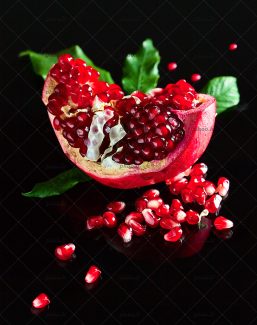 عکس با کیفیت پس زمینه به رنگ مشکی و انار نصف شده با دانه های قرمز