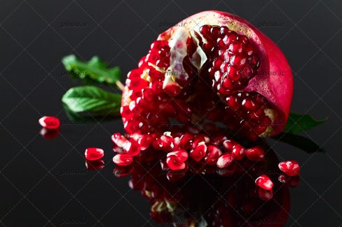 عکس با کیفیت دانه های قرمز انار در کنار انار نصف شده و بکگراند به رنگ مشکی
