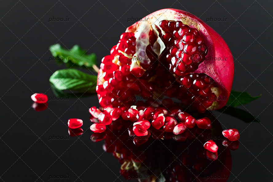 عکس با کیفیت دانه های قرمز انار در کنار انار نصف شده و بکگراند به رنگ مشکی