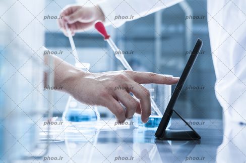 عکس با کیفیت پزشک در حال کار کردن با آیپد و چند شیشه آلات آزمایشگاهی در اطراف