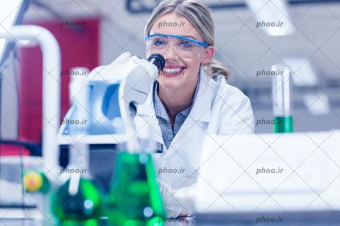 عکس با کیفیت پزشک آزمایشگاه خوش چهره همراه با عینک ایمنی و در حال تست و آزمایش به کمک شیشه آلات آزمایشگاهی
