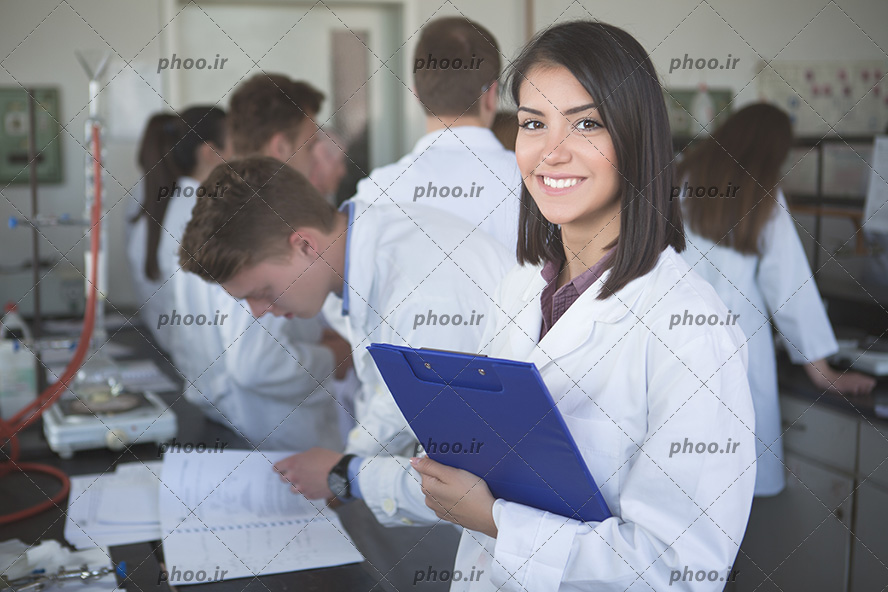 عکس با کیفیت دانشجوی پزشکی با روپوش سفید و لبخند زیبا ایستاده در کنار دیگر دانشجوها