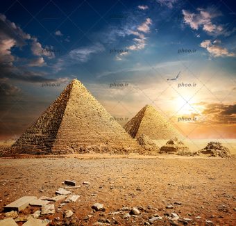 عکس با کیفیت اهرام مصر در کنار یکدیگر و هرم های کوچک تر خراب شده در کنارشان و پرنده ای در حال پرواز در بالای آنها و آسمان زیبا در پس زمینه