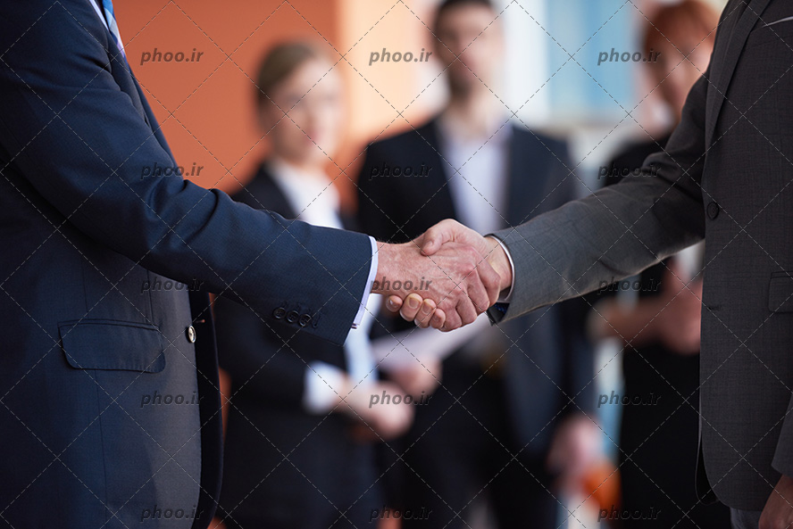عکس با کیفیت دو مرد با کت و شلوار در حال دست دادن به یکدیگر در مقابل افراد دیگر