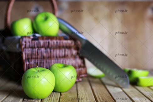 سیب های سبز تازه در سبد به همراه چاقو و سیب قاچ خورده