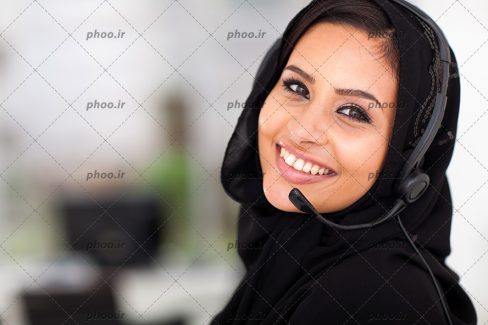 عکس یک خانم با شال مشکی که هدست بر گوش دارد و در حال خندیدن است