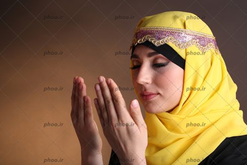 عکس یک خانم با حجاب با شال زرد و هدبند که چشم های خود را بسته و در حال دعا کردن است