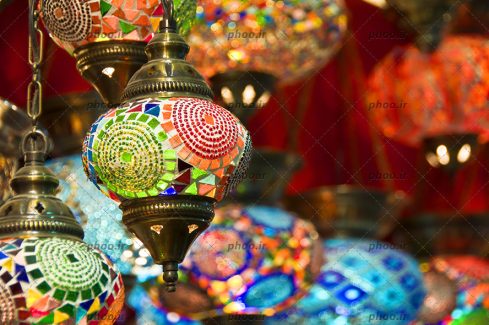 عکس لوستر های رنگی که از سقف آویزان است و شیشه های آن با آینه و منجق کار شده است