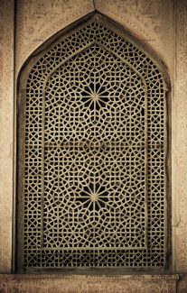 عکس یک پنجره ی چوبی با شکل های هندسی روی آن و نمای اطراف آن که از سنگ است