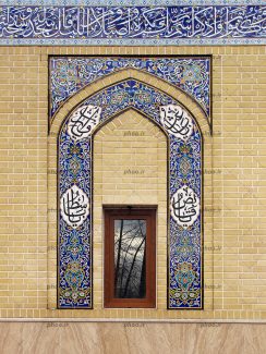 عکس یک پنجره مستطیلی باشیشه ای که عکس درختان روی آن افتاده و نمای آجری و کاشی های آبی که روی آن نوشته های قرآنی دارد
