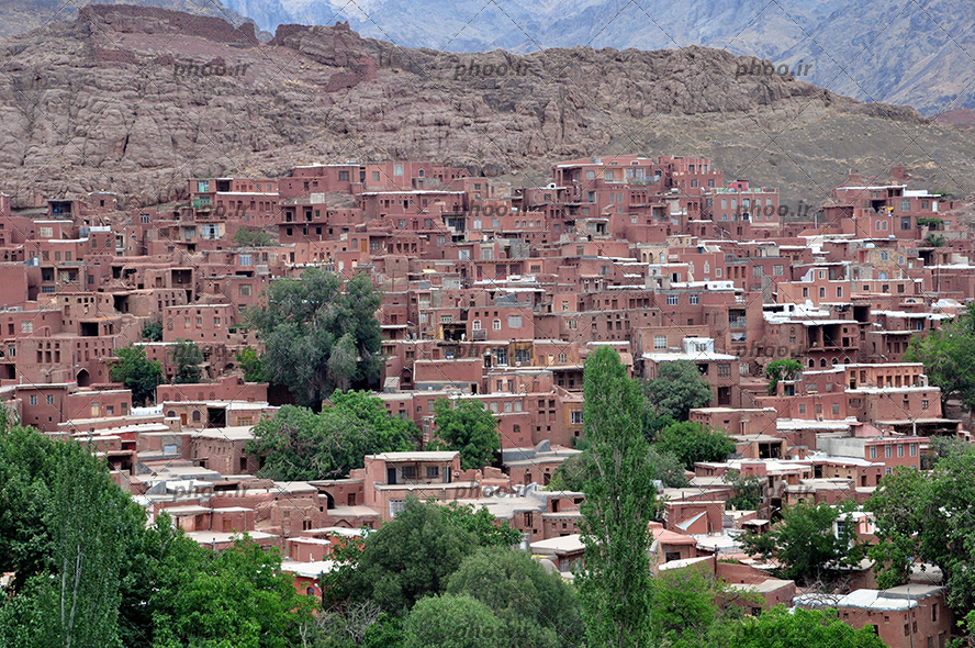 عکس یک روستا با خانه های گلی و پلکانی در دامنه کوه با درختان سرسبز