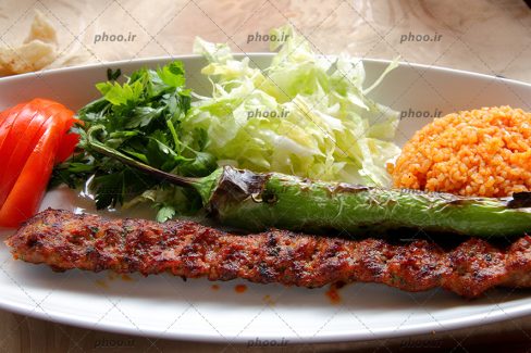 عکس یک دیس غذا از کباب کوبیده ، برنج کته و فلفل کبابی و سبزیجات کنار آن