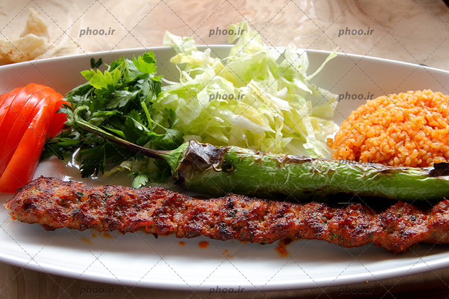 عکس یک دیس غذا از کباب کوبیده ، برنج کته و فلفل کبابی و سبزیجات کنار آن
