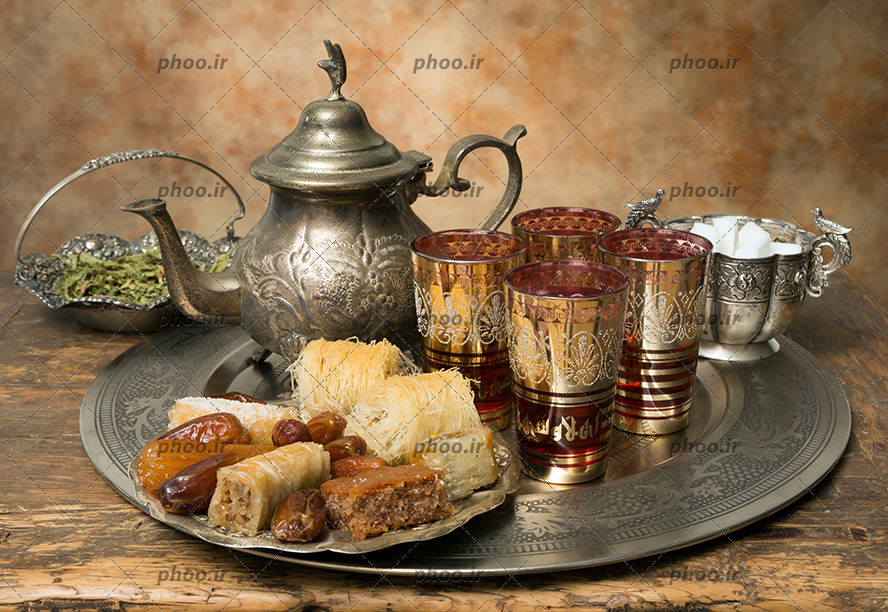 عکس یک سینی که در آن یک بشقاب شیرینی و استکان چای ، قندان و قوری دمنوش دارد