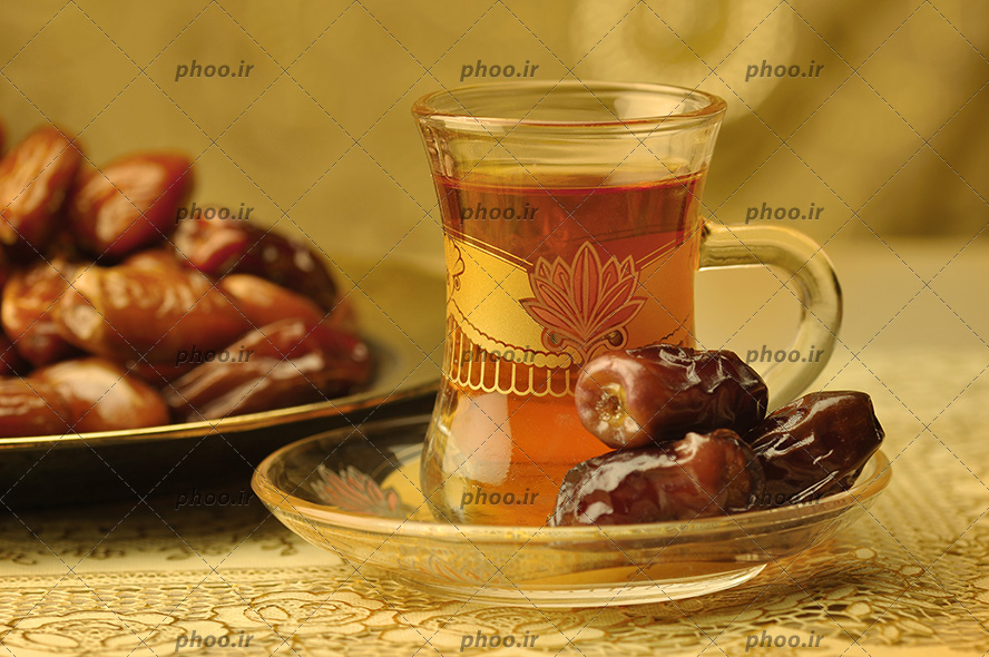 عکس یک استکان چای و خرما روی نعلبکی و یک بشقاب خرما