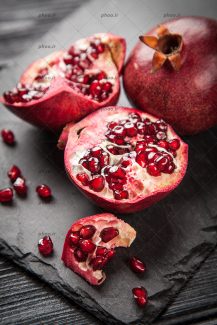 عکس زیبا از یک انار و یک انار قاچ شده روی تکه سنگ