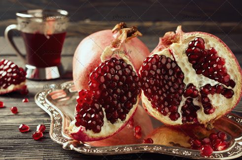عکس زیبا از انار رسیده و خوشرنگ قاچ شده به همراه انار روی سینی در پس زمینه آب انار در استکان