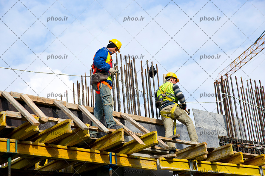 کارگران و مهندسین ساختمان در ارتفاع در حال کار کردن بالای ساختمان با لباس مخصوص و کلاه ایمنی