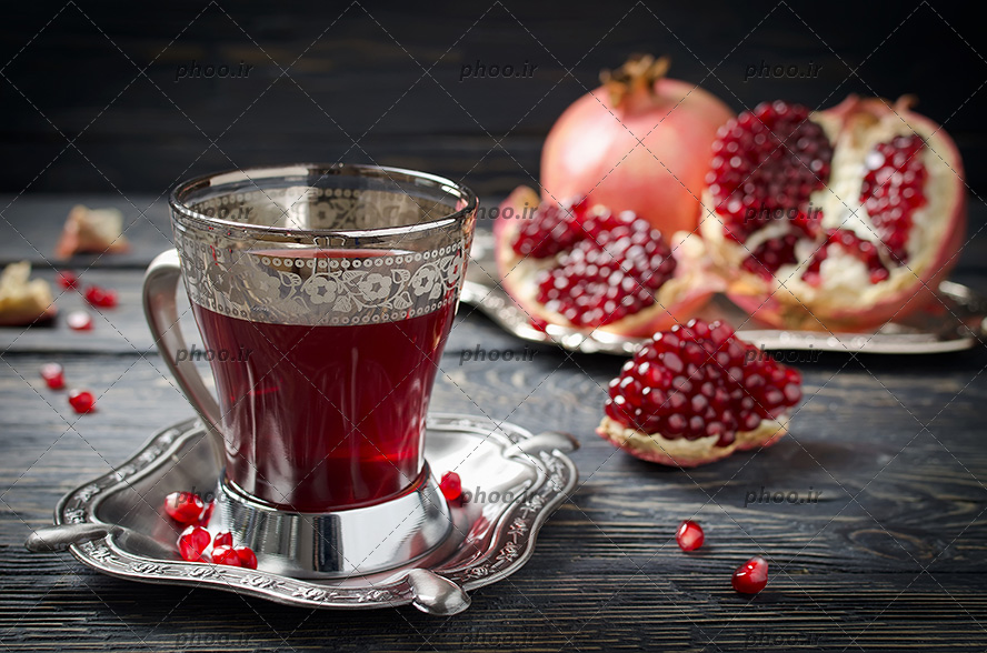 انار به همراه انار نصف شده در پیش زمینه چوبی و دانه های ریخته شده به همراه چای